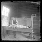 Man standing over a dead body laid out on a table